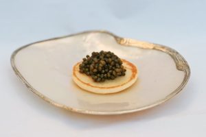 Beispiel für Kaviarsorten: Osietra Kaviar auf einem Miniblini, serviert auf einer Muschelschale mit Goldrand.