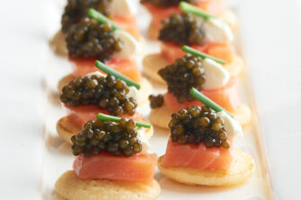 acht Blinis, belegt mit filletiertem Räucherlachs und Kaviar, garniert mit Crème Fraîche und Schnittlauch